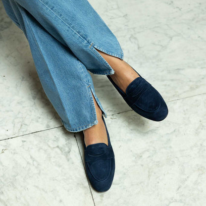 Suede Navy loafers worn with blue jeans on a tiled floor.
