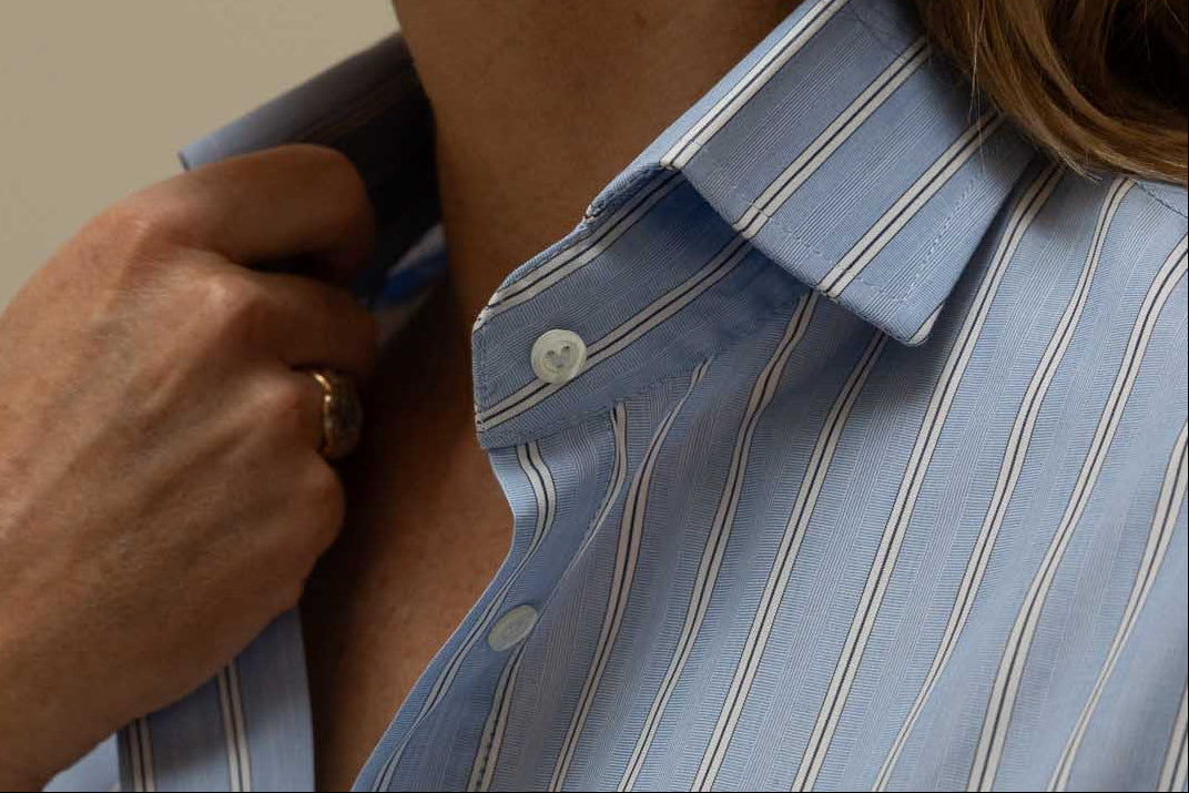 Woman adjusting her collar wearing a light blue striped shirt.