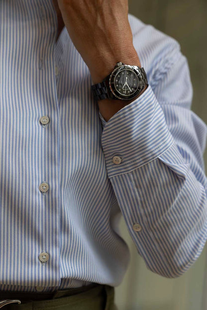 Close-up of a wrist wearing a watch with a blue striped shirt.
