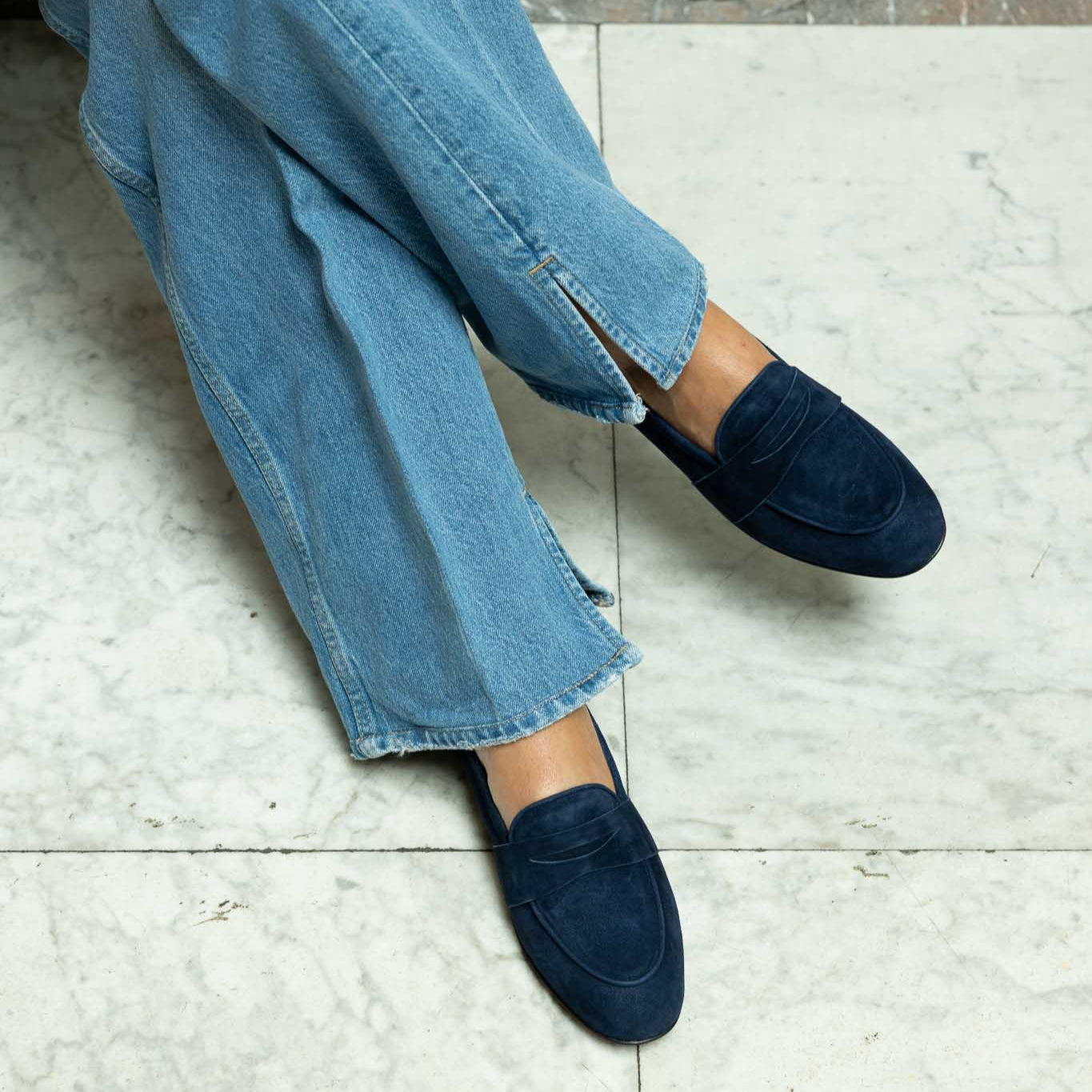 woman wearing blue jeans and navy loafers on a tiled floor