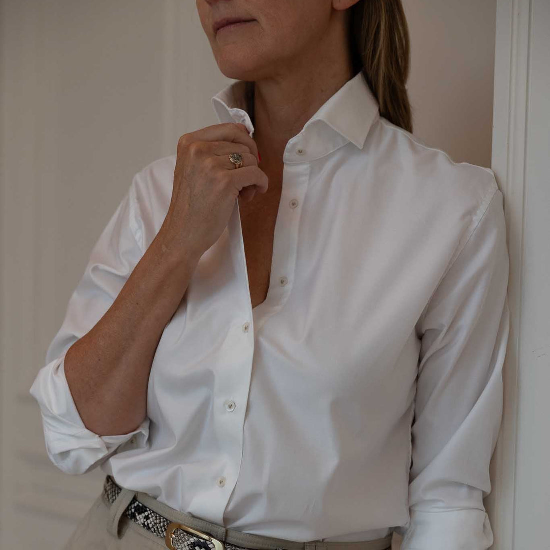 Person wearing a white shirt and beige pants with a belt, standing against a plain background.