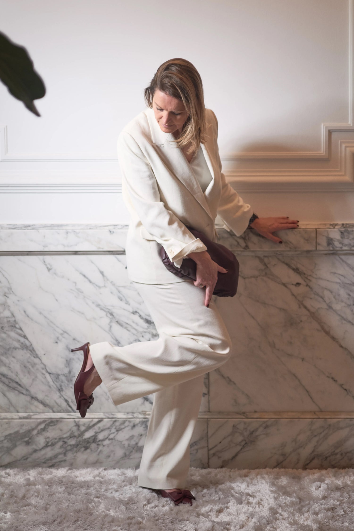 Woman in a white outfit posing on a marble staircase looking at her bordeaux kitten heels